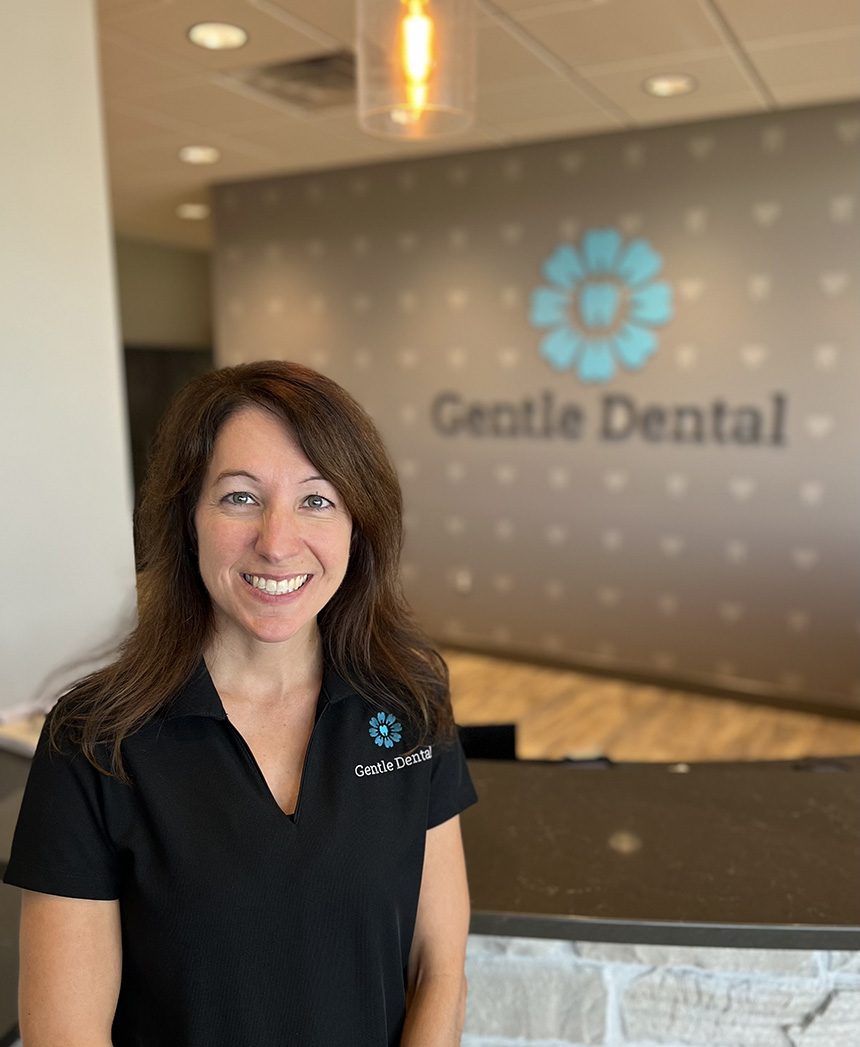 The image shows a woman standing in front of a sign with the text Gentle Dental on it, posing for a photograph.