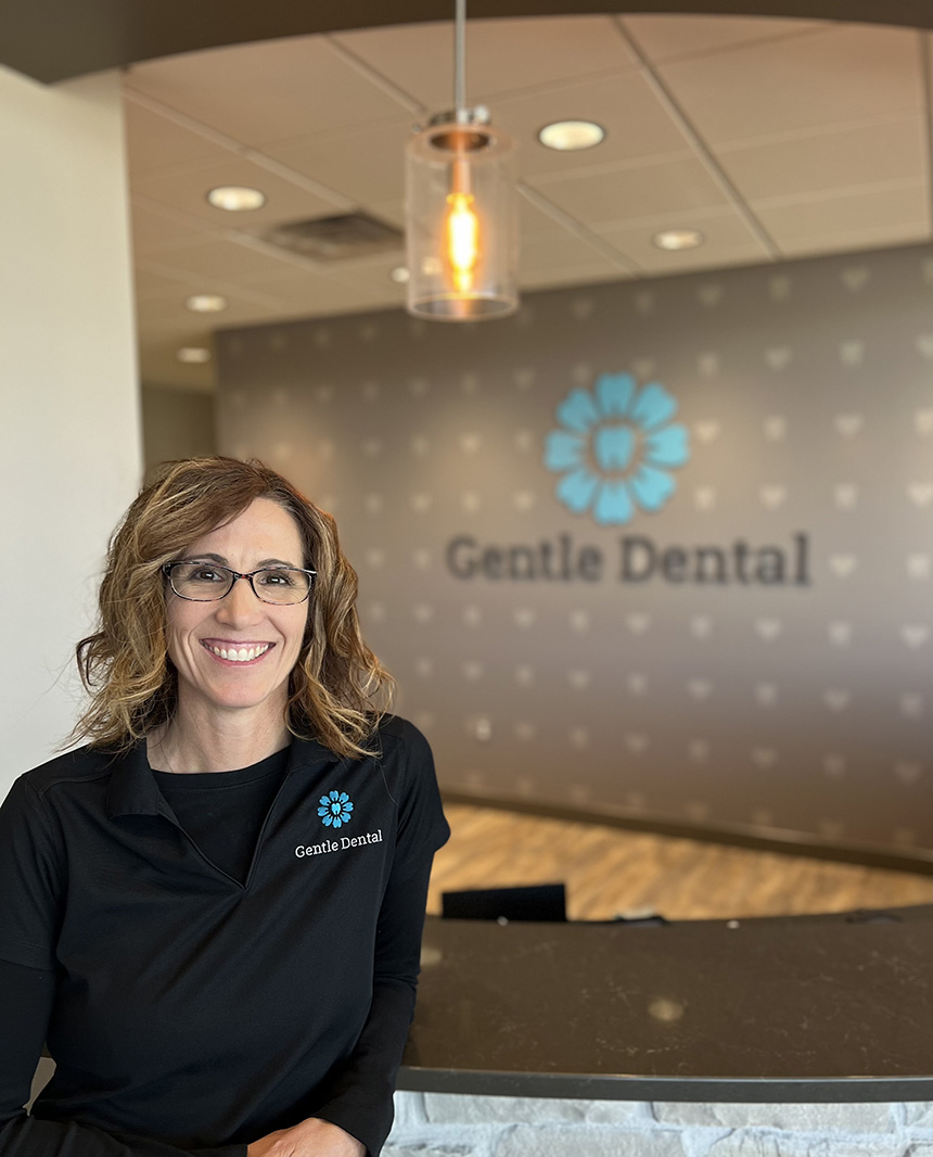 A woman standing in front of a sign for Gentle Dental in an office setting.
