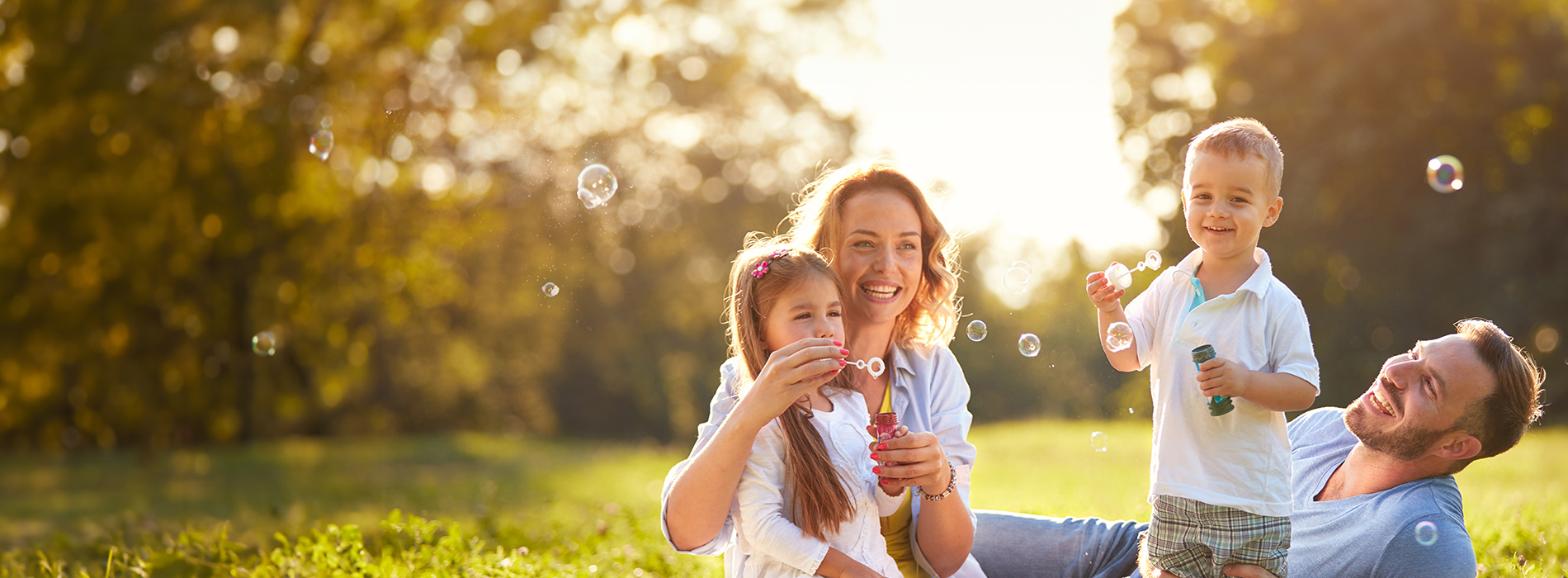 A family of four enjoying a sunny day outdoors with bubbles, including two adults and two children, with a backdrop of a clear sky.